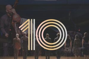 Multiple artists on stage, a large number 10 is superimposed above them